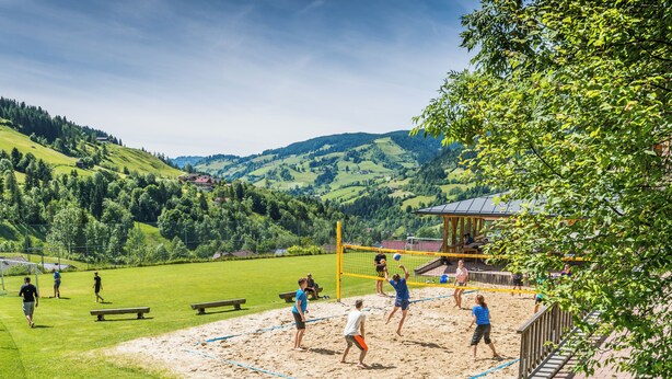 A volleyball court with players, benches, and a pavilion in a hilly landscape. - Arrive.feel good.enjoy (Wagrain)