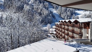 A snow-covered mountain landscape with a building featuring wooden balconies and a ski slope in the background. - Arrive.feel good.enjoy (Wagrain)