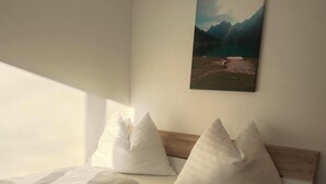 A neatly made bed with white bedding and pillows, a wooden headboard, and a painting of a landscape on the wall. - Arrive.feel good.enjoy (Wagrain)