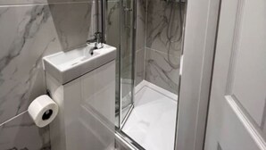 Et moderne badeværelse med bruseniche i glas, marmorfliser og en hvid vask.