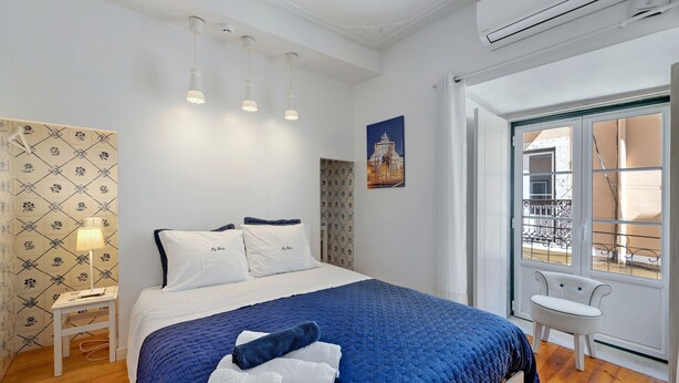 Een slaapkamer met een bed, nachtkastje, stoel, raam met uitzicht en een airconditioning.