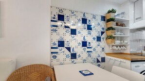 Een keuken met een witte tafel, een rieten stoel en blauw-witte betegelde vloeren.