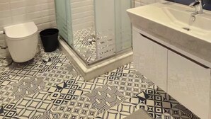 Une salle de bain moderne avec une douche à parois de verre, des toilettes blanches, une poubelle noire et un lavabo avec un miroir au-dessus.