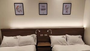 Une chambre d’hôtel avec deux lits, une tête de lit en bois et trois œuvres d’art encadrées accrochées au mur.