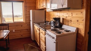 Una cocina compacta con paredes de madera, un refrigerador, un microondas, una estufa y una cafetera.