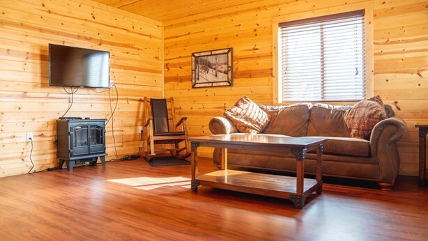 Interior de una cabaña de madera con un sofá, una mesa, un televisor y una chimenea.