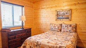 Una habitación de cabaña de madera con una cama, un tocador y un cuadro en la pared.