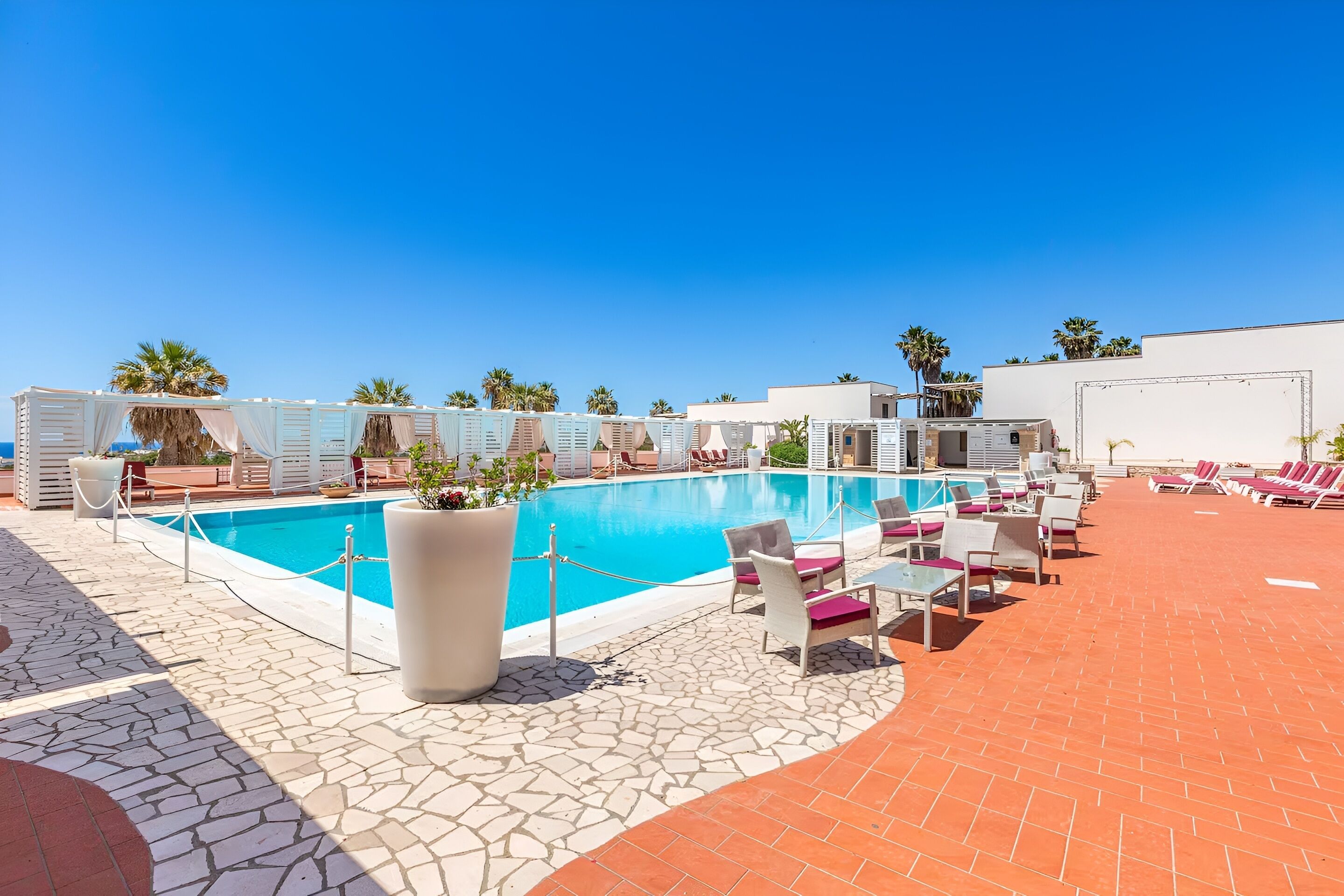 A pool area with lounge chairs and a clear blue sky.