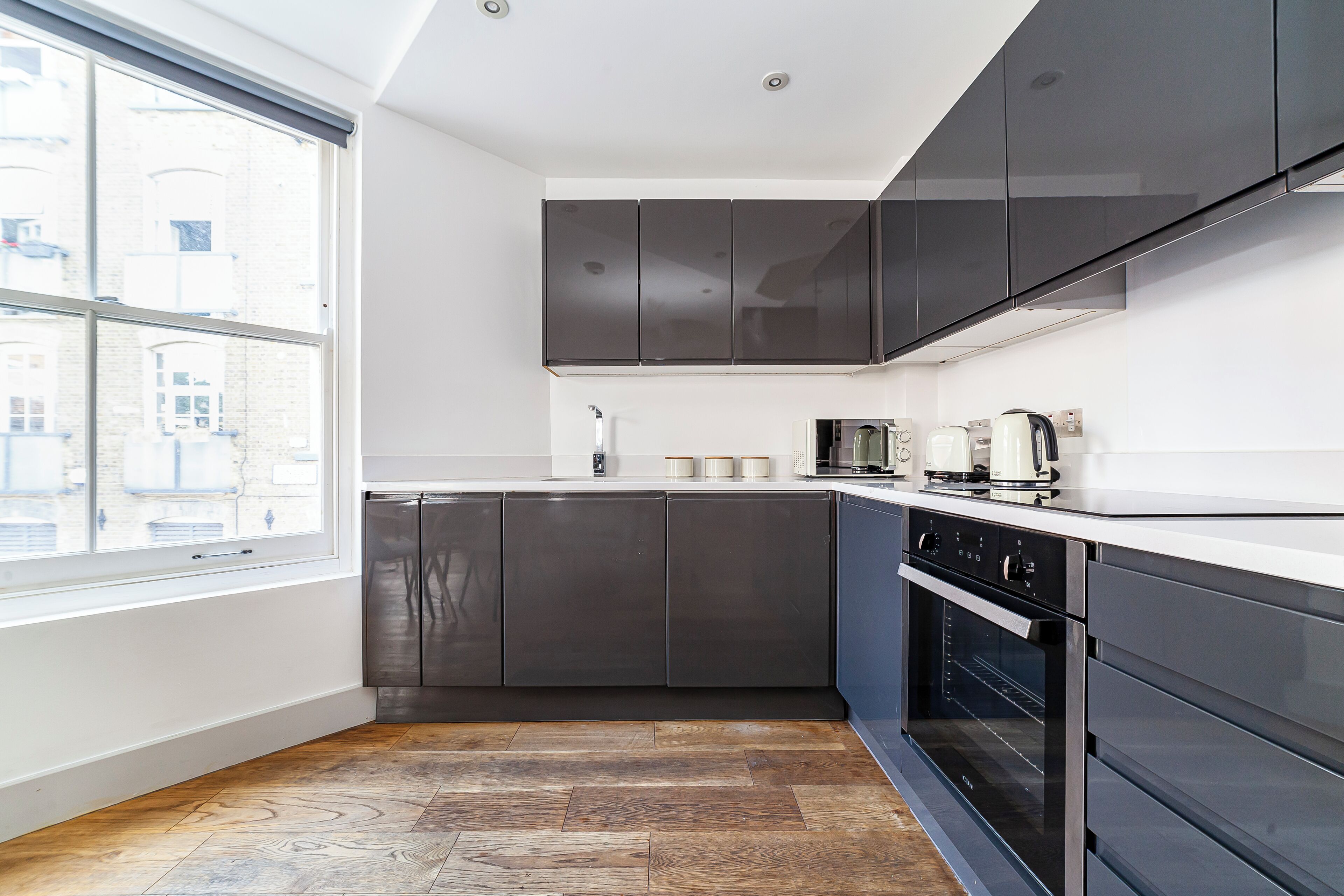 A modern kitchen with dark cabinets, a large window, and a built-in oven.