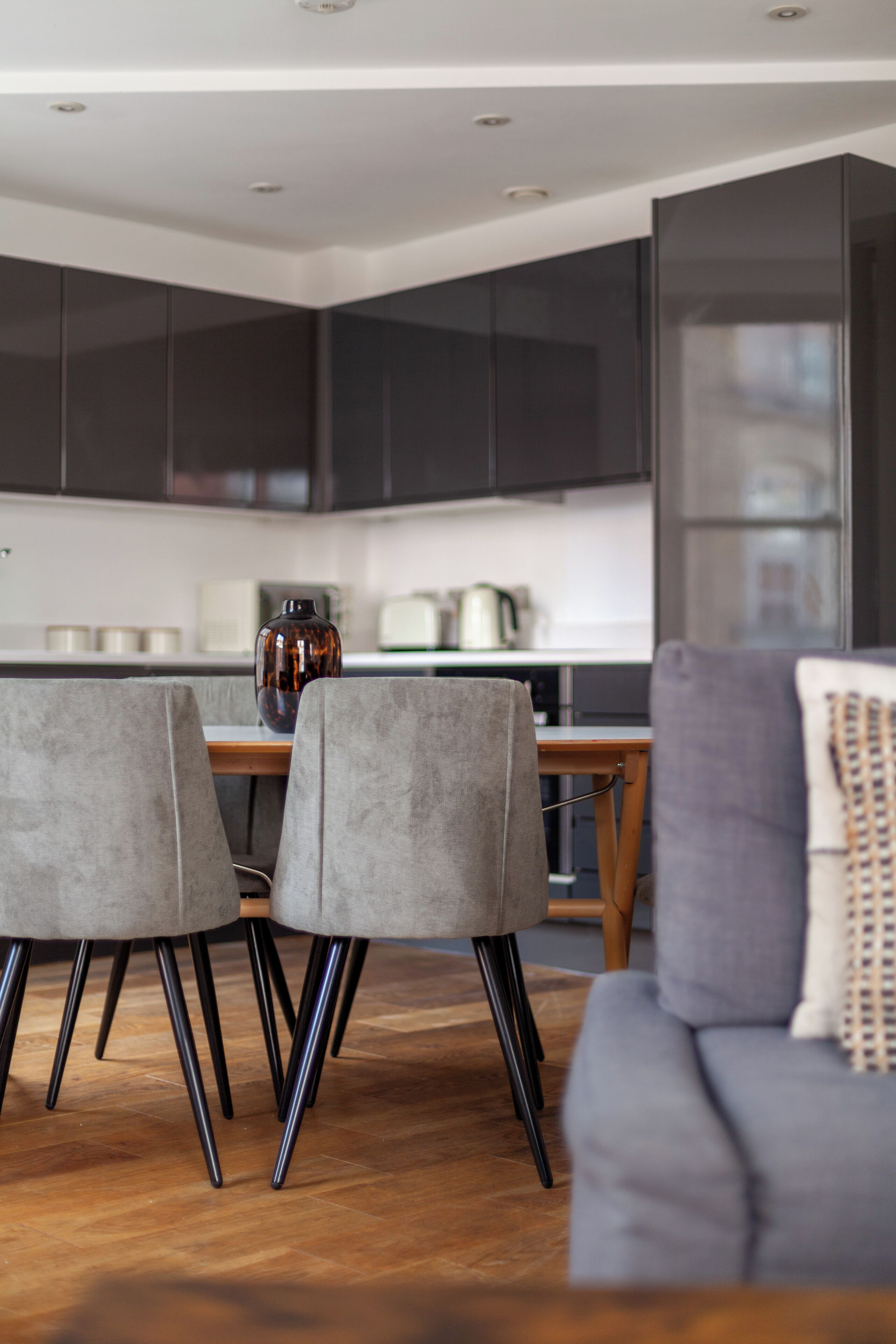 A modern kitchen with dark cabinets, a wooden dining table, and a vase on the table.