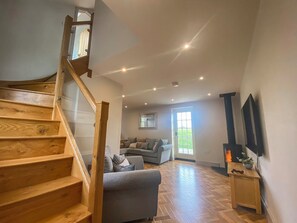 Un vaste espace de vie agrémenté d’un escalier en bois, d’un canapé gris et d’un téléviseur fixé au mur.
