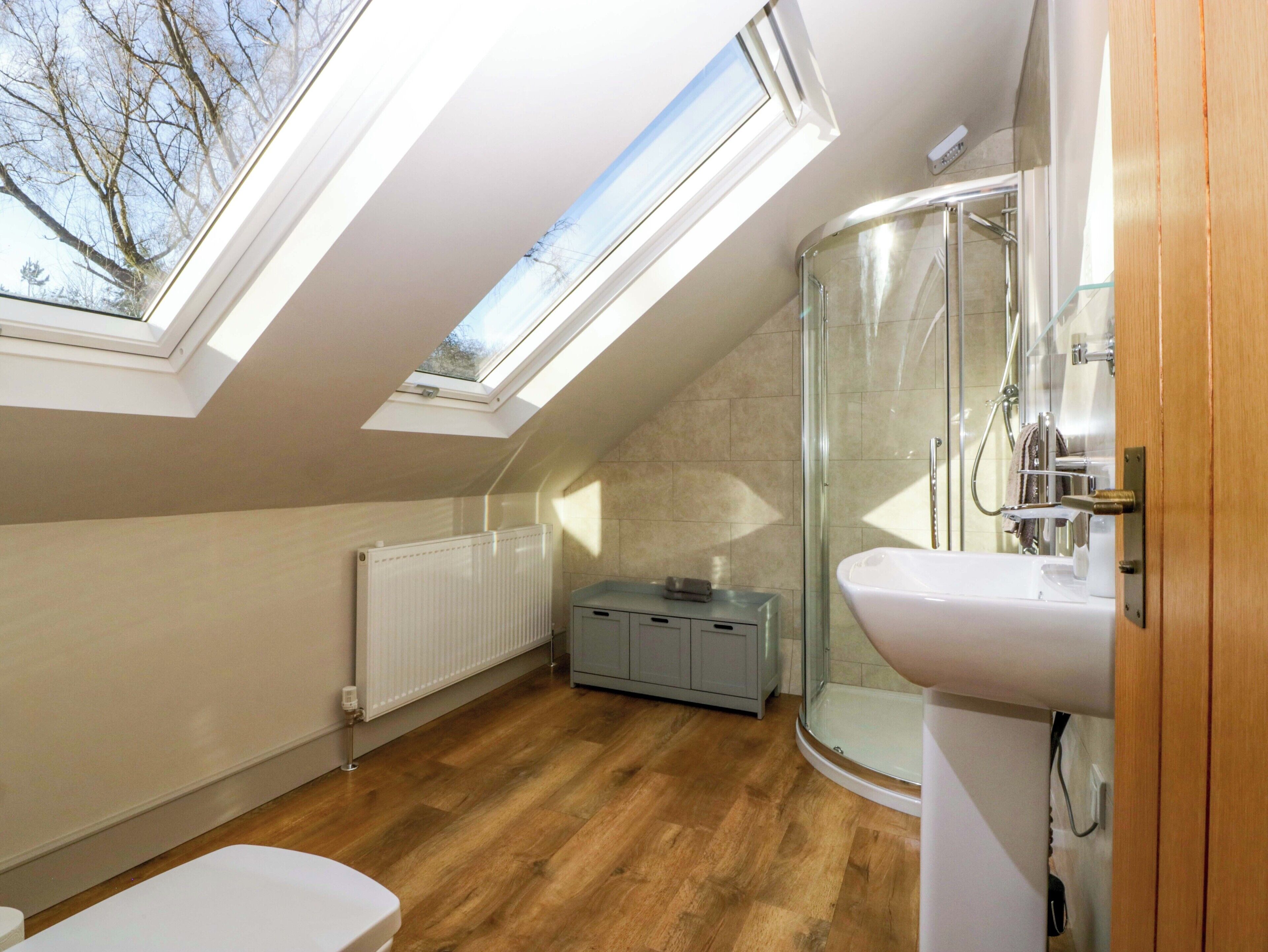 A modern bathroom with skylights, a glass shower, and a wooden floor.