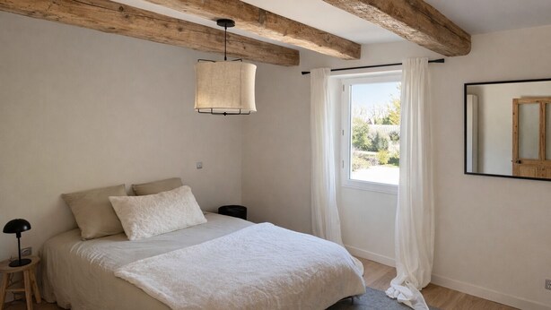 Um quarto com cama, luminária pendente, janela com cortinas e espelho na parede.