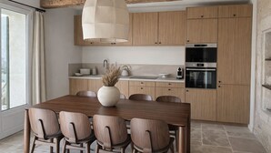 Cozinha moderna com armários de madeira, mesa de jantar com cadeiras, luminária pendente e janela com cortinas.