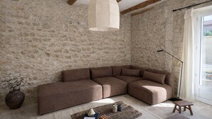 Quarto com parede de pedra, sofá seccional marrom, mesa de centro de madeira e luminária pendente.