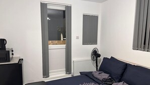 Ein Zimmer mit Bett, Schreibtisch, Stuhl, einem Fenster mit Vorhängen und einer Heizung.