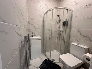 A modern bathroom with a glass-enclosed shower, a white toilet, and a small cabinet. - Buckingham Palace/Hyde Park near (Greater London)