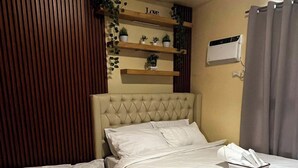A hotel room with a double bed, a single bed, a wooden slat wall, a shelf with plants, and a wall-mounted air conditioner. - Your Home Away From Home | Journey & Rest Staycation (Bacolod)