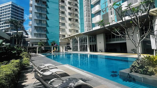 A swimming pool with lounge chairs, surrounded by tall residential buildings. - Your Home Away From Home | Journey & Rest Staycation (Bacolod)