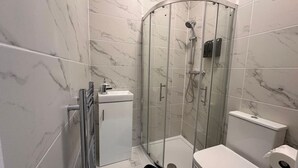 Een moderne badkamer met een douchecabine van glas, een wit toilet en een klein kastje.