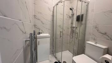 A modern bathroom with a glass-enclosed shower, a white toilet, and a small cabinet.