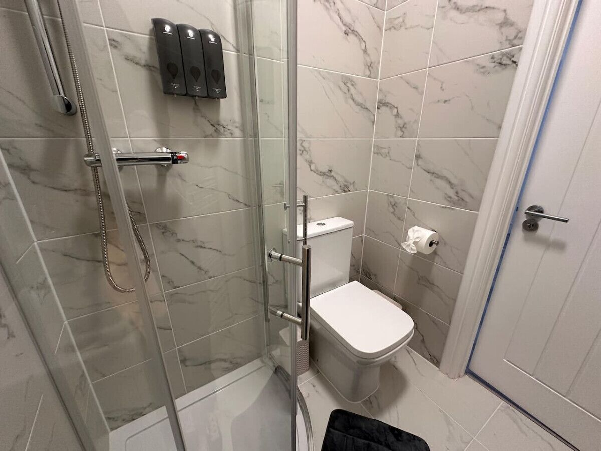 A bathroom with a glass-enclosed shower, a toilet, and a hand dryer.