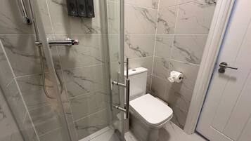 A bathroom with a glass-enclosed shower, a toilet, and a hand dryer.
