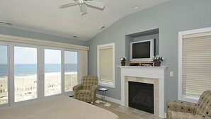 A bedroom with a large bed, a fireplace, a television, and a ceiling fan. - Oceanfront 3BR Condo in Fenwick | Walk to Beach! (Fenwick Island)