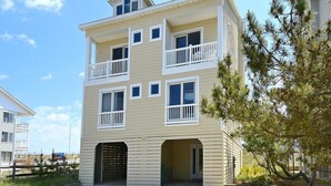 A multi-story building with a balcony on the second floor, a garage entrance, and a clear sky. - Oceanfront 3BR Condo in Fenwick | Walk to Beach! (Fenwick Island)