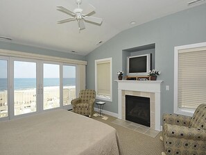 A bedroom with a large bed, a fireplace, a television, and a view of the beach. - Oceanfront 3BR Condo in Fenwick | Walk to Beach! (Fenwick Island)