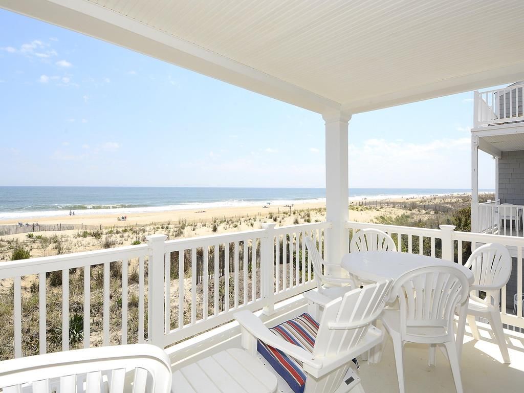 Un espace extérieur abrité, doté de mobilier blanc, offrant une vue sur la plage et s’ouvrant sur un ciel dégagé.