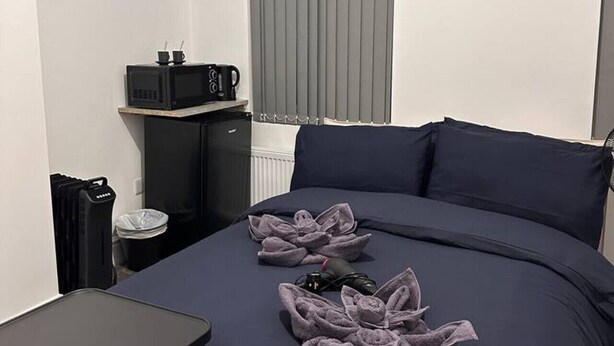 A bedroom with a bed, a small table, a radiator, and a window with blinds. - London Vauxhall/Victoria room (Greater London)