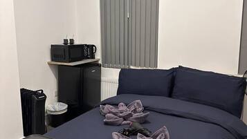 A bedroom with a bed, a small table, a radiator, and a window with blinds.