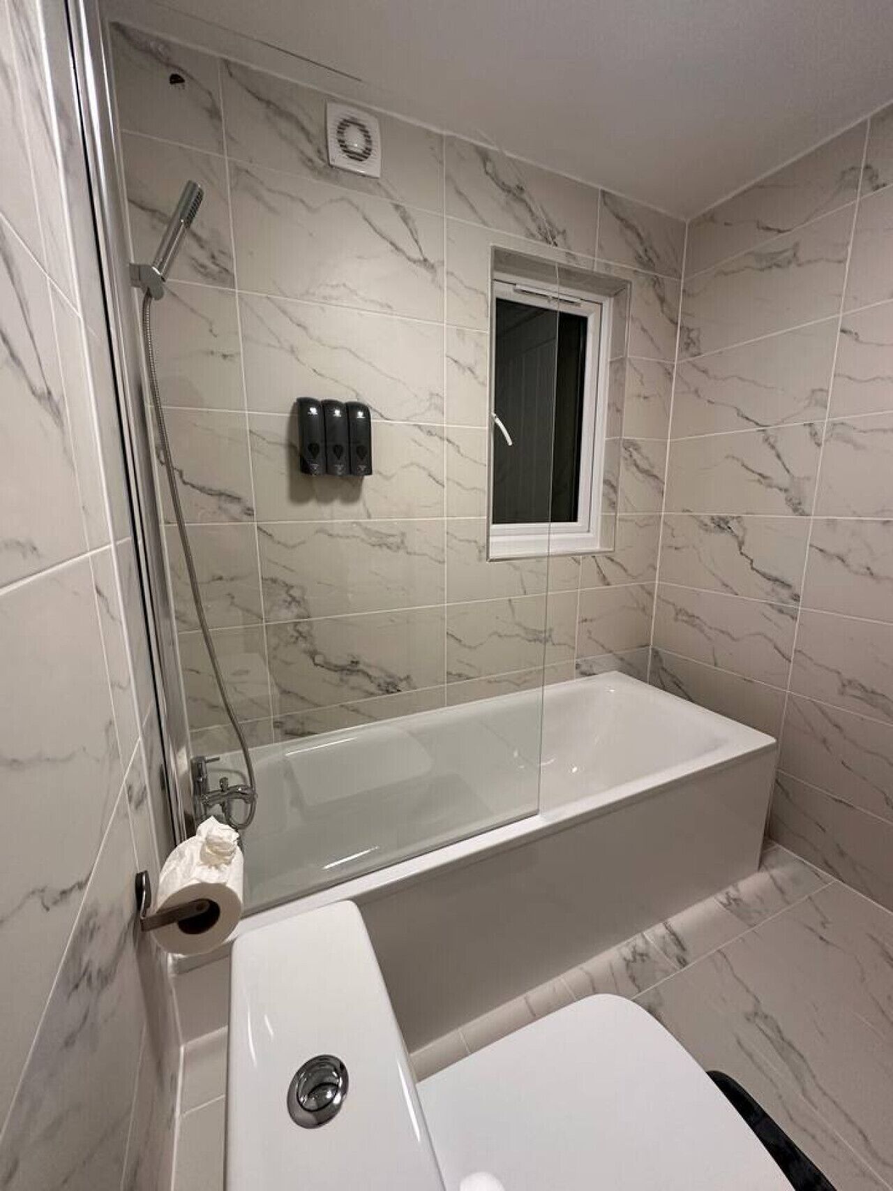 A modern bathroom with a glass-enclosed shower, a white bathtub, and a small window.