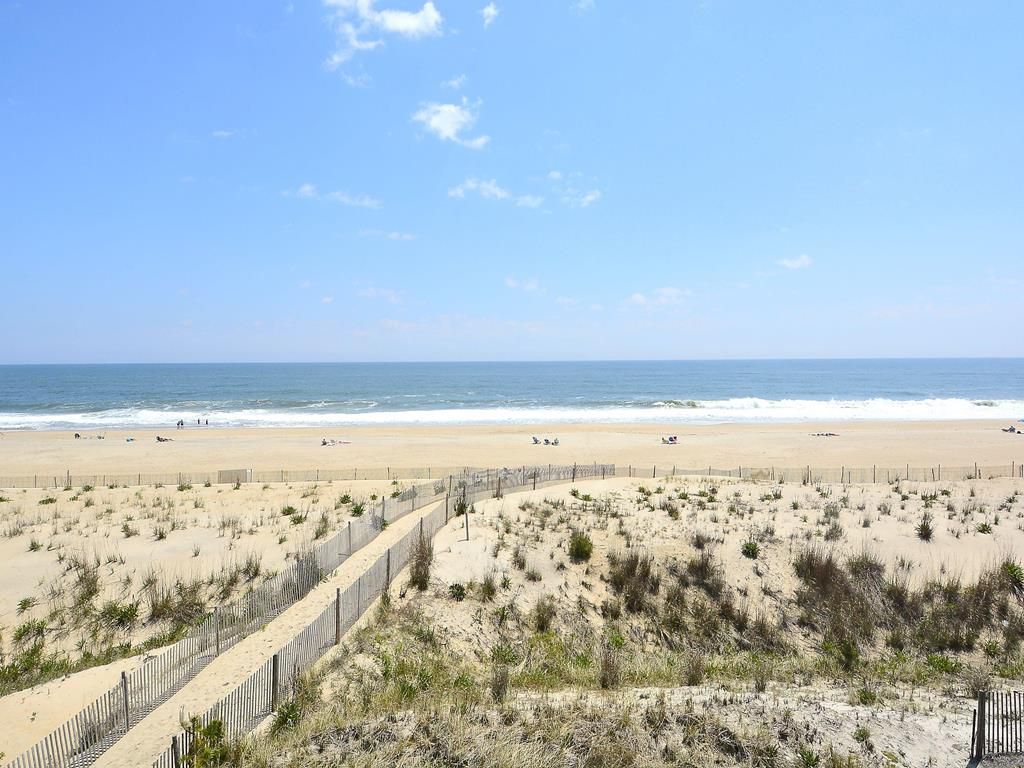 A beach with a fence, sandy dunes, and the ocean in the background.