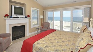 Ein Schlafzimmer mit Kamin, Fernseher, Bett mit rotem Läufer, Sessel und Blick auf den Strand.