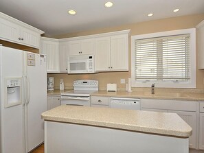 A kitchen with white cabinetry, a microwave, a stove, a sink, and a window with blinds. - Oceanfront 3BR Condo w/ Views + Grill | Sleeps 8! (Fenwick Island)