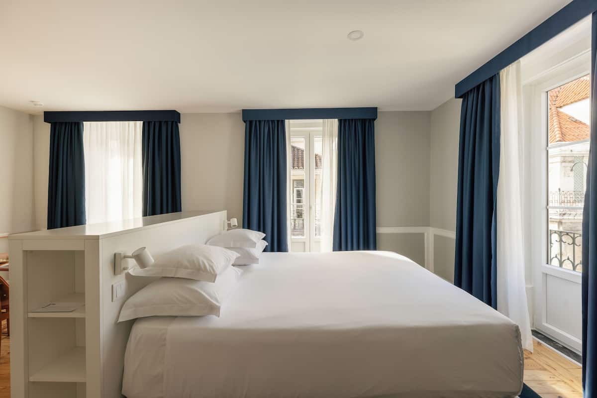 Ein Hotelzimmer mit Bett, Nachttisch, Sessel und Blick ins Freie.