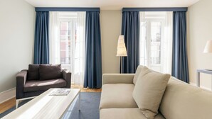 A modern living room with a brown leather sofa, a beige sofa, a white coffee table, and a lamp. - Esqina Apartments (Lisbon)