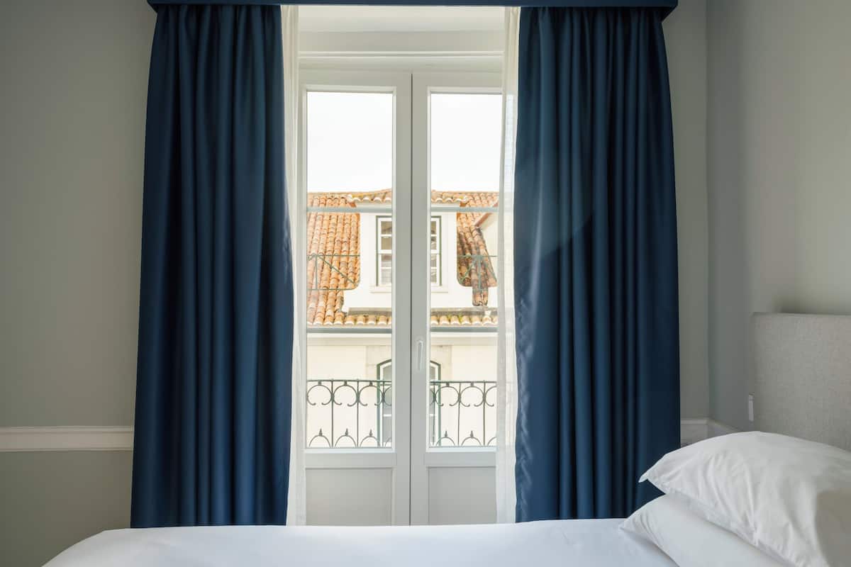Ein Zimmer mit einem Bett, einem Vorhangfenster und Blick auf einen Balkon mit Geländer.