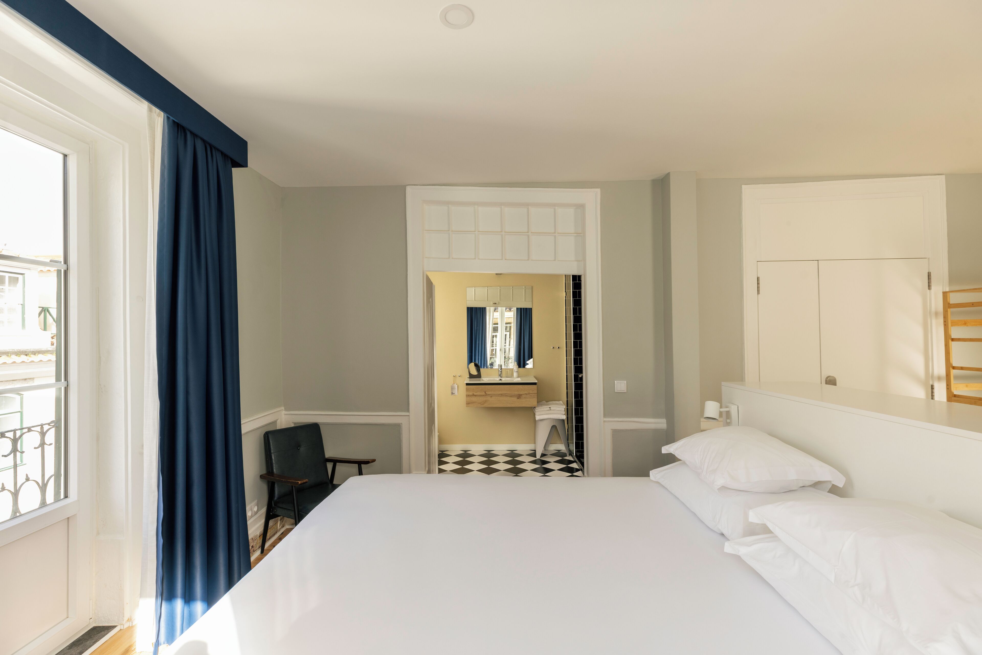 A hotel room with a bed, a chair, a bathroom with a mirror, and a view of the outside.
