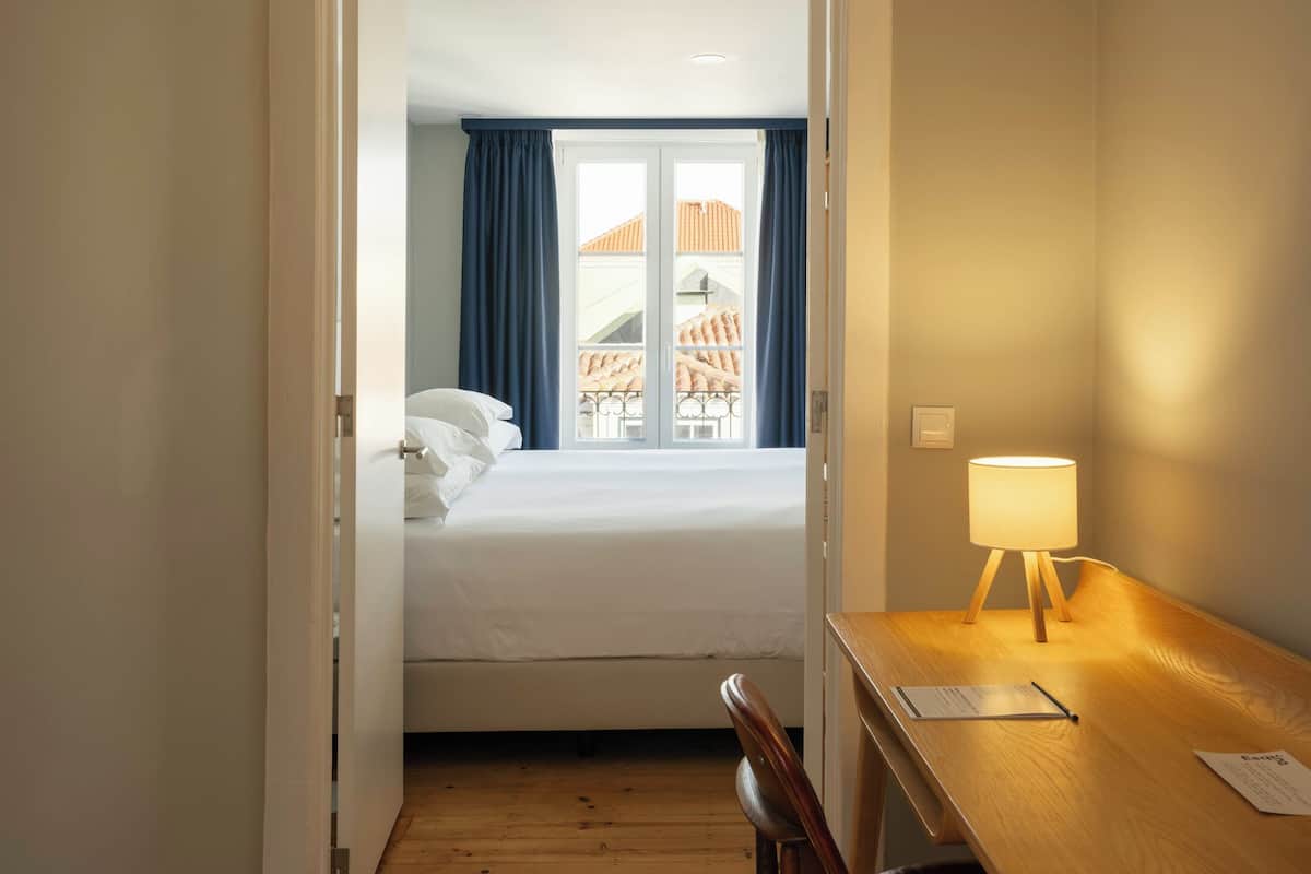 Ein Hotelzimmer mit einem Holztisch, einem Stuhl, einem Bett und einem Fenster mit Vorhängen.