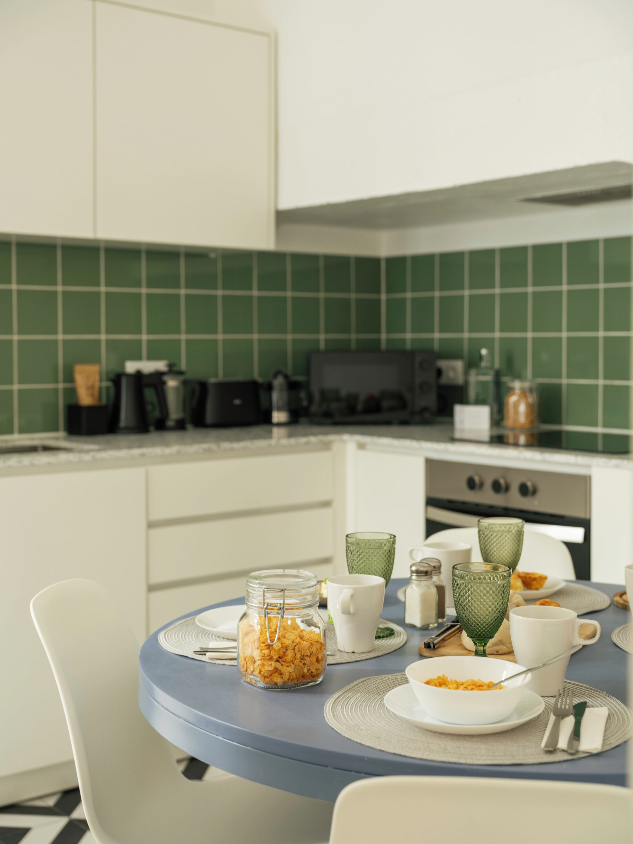 A modern kitchen with a blue table, white chairs, and a green tiled backsplash.