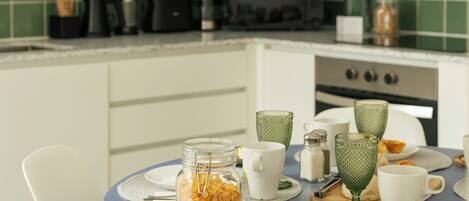 A modern kitchen with a blue table, white chairs, and a green tiled backsplash.