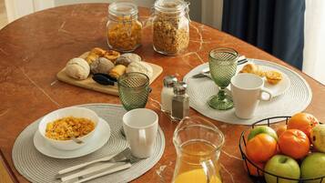 Una mesa de desayuno con diferentes alimentos, una jarra de jugo de naranja y una cesta de frutas.