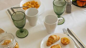 A breakfast setting with a plate of pastries, a bowl of cereal, and a glass jar of cereal flakes.