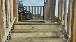 Una escalera de madera que lleva a un porche cubierto con una mecedora y vistas del entorno.