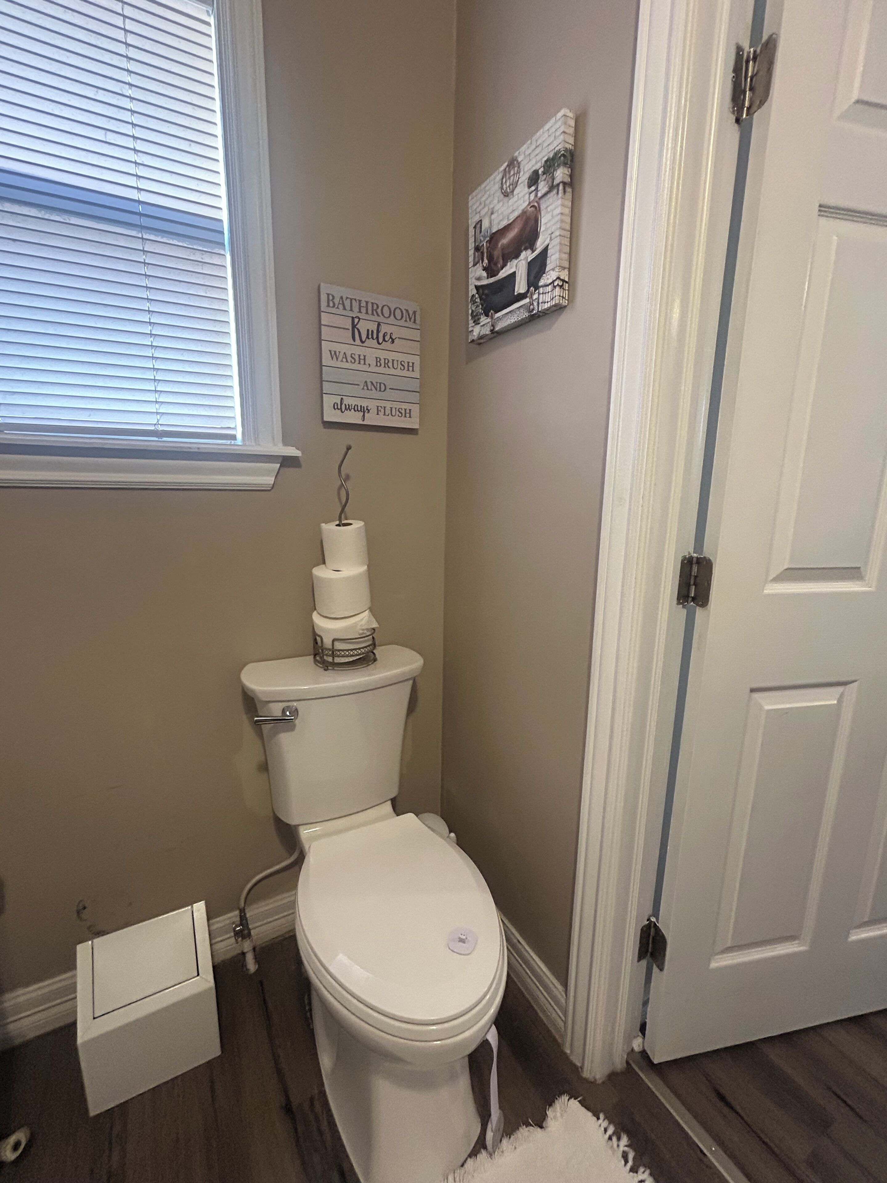A bathroom with a toilet, a wall-mounted toilet paper holder, and a sign with bathroom rules.