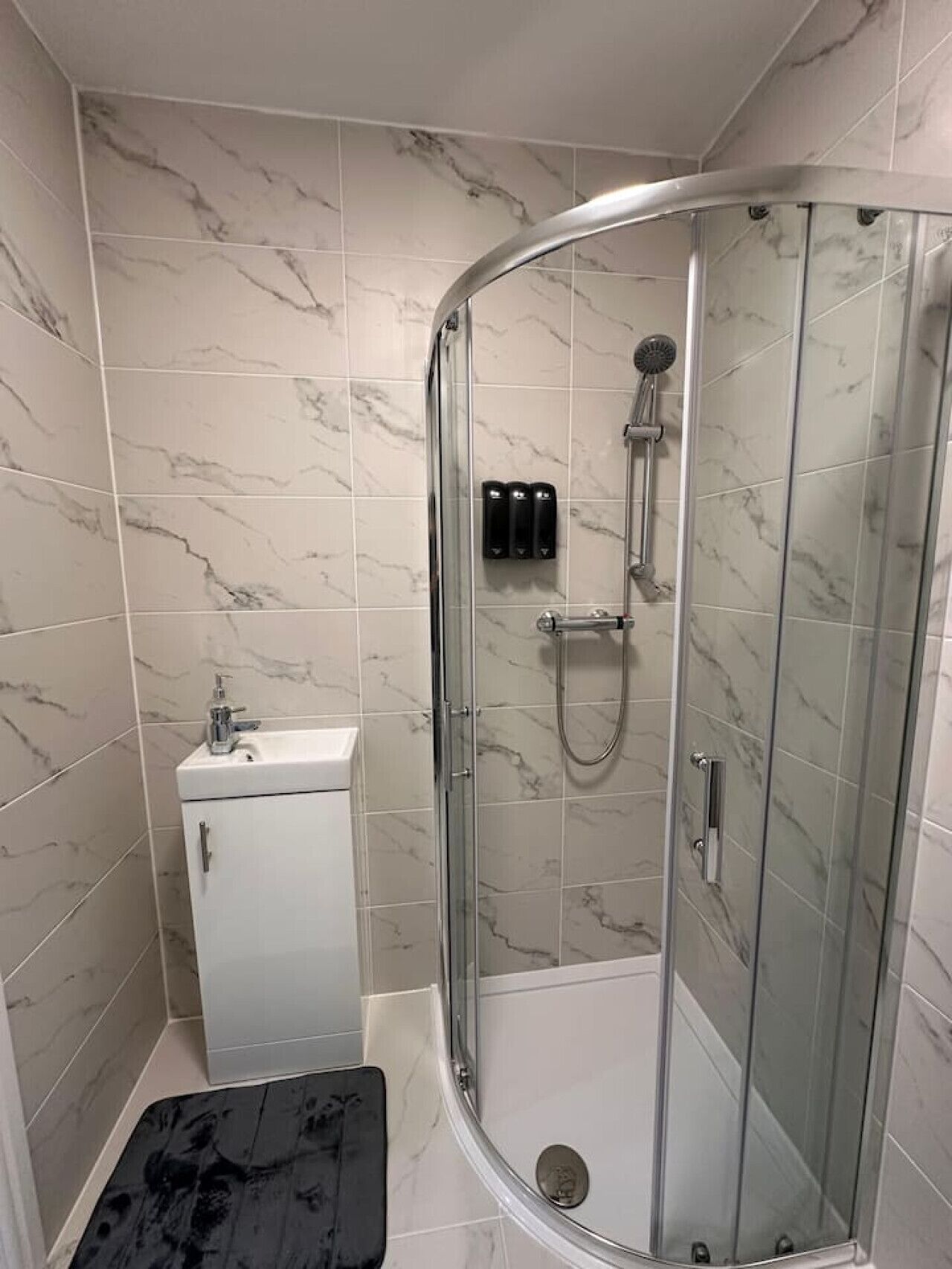 A modern bathroom with a glass-enclosed shower, a white sink, and a small cabinet.