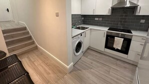Cocina compacta con lavadora, horno y una escalera que sube a otra habitación.